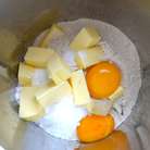Для приготовления теста используем кухонный комбайн. В чашу миксера положите муку, кусочки охлажденного сливочного масла, яичные желтки,  мелко натертую цедру половины лимона, сахарную пудру и щепотку соли. Включите комбайн и в течение нескольких секунд измельчите все до состояния мокрой крошки.