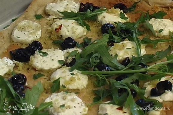 Готовую пиццу посыпать измельченными листьями базилика, руколой, сбрызнуть оставшимся оливковым маслом и лимонным соком.