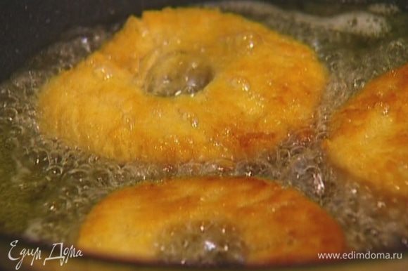Разогреть в глубокой тяжелой сковороде растительное масло и обжарить пончики с двух сторон.