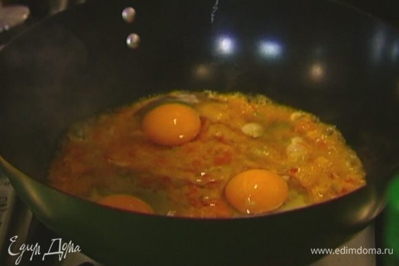 Разогреть сухую глубокую сковороду, выложить в нее овощи (3 ст. ложки оставить), разбить сверху яйца.