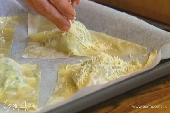 Противень выстелить бумагой для выпечки, выложить пирожки, смазать их оставшимся сливочным маслом и посыпать натертым сыром.