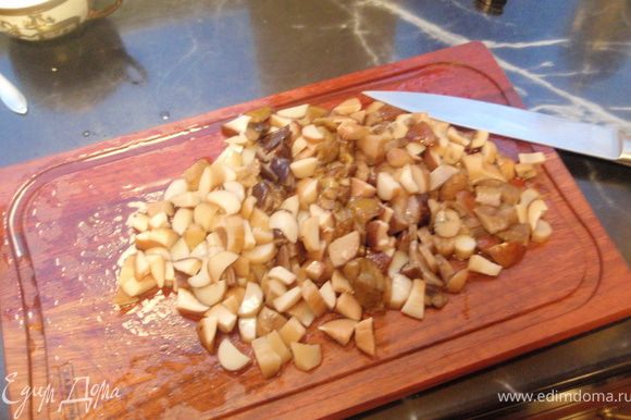 Отваренные грибы довольно мелко режем. И отправляем сначала на сухую сковороду, когда лишняя влага уйдет, добавляем масло и половину нашинкованного лука. Обжариваем до золотистости.