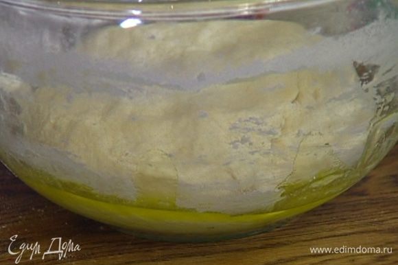 Выложить тесто на рабочую поверхность, присыпанную мукой, и слегка вымесить, затем уложить снова в посуду, смазанную оливковым маслом, накрыть влажным полотенцем и оставить еще на 10 минут.