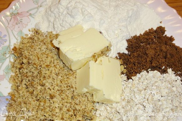 Орехи измельчите в блендере. Масло желательно предварительно подержать в морозильной камере и порезать кусочками. Из масла, сахара, муки, хлопьев и орехов приготовьте крошку.