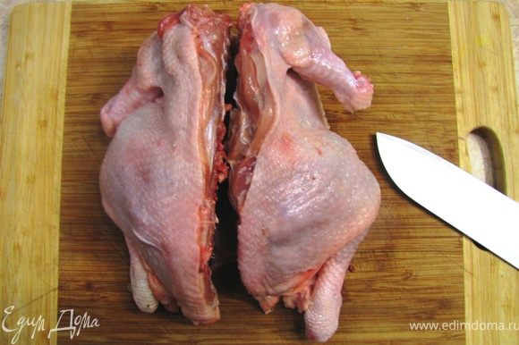 Промойте и обсушите курицу кухонным полотенцем. Положите курицу на разделочную доску грудкой вниз. Срежьте лишние кости с крыльев, как показано на фотографии. Разрежте курицу вдоль позвоночника.
