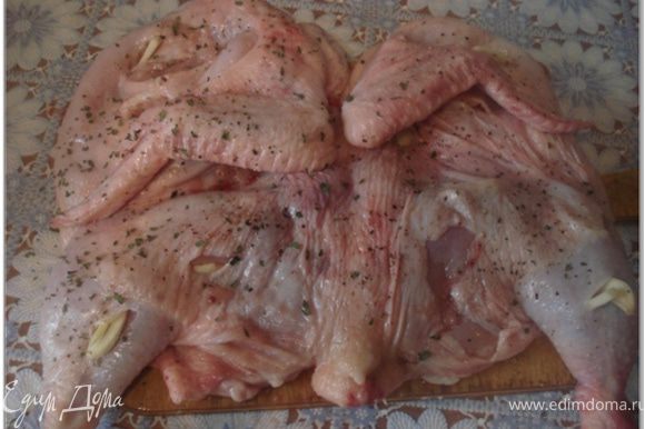 Цыпленка тщательно вымыть, обсушить и при необходимости обпалить. Положить цыпленка на разделочную доску и осторожно разрезать вдоль грудки. Чеснок очистить. 2 зубчика чеснока разрезать примерно на 10 тонких долек. Остальной чеснок мелко нарубить или пропустить через ручной пресс. Цыпленка хорошо отбить с обеих сторон, натереть солью, молотым красным и черным перцем. Сделать на коже небольшие надрезы и нашпиговать их дольками чеснока.