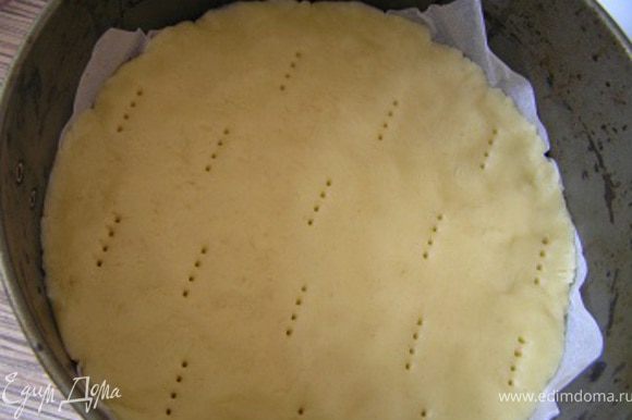 Форму для выпечки застелить пекарской бумагой, распределить тесто, проколоть вилкой в нескольких местах.