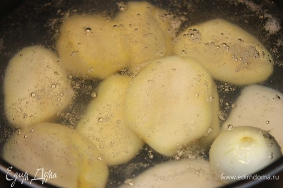 Картофель почистить, опустить в слегка подсоленную кипящую воду, туда же положить 1 небольшую луковку целиком.