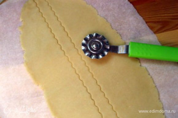 Снова раскатать срезанное тесто. Это удобно делать между двух листов пергамента. Колёсиком с зигзагом нарезать тесто на полоски. Взбить яйцо.