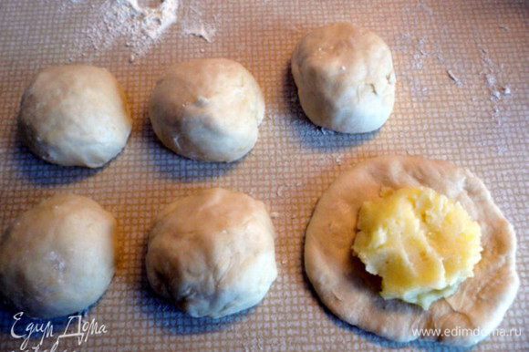 Делим тесто на две неравные части. 1/3 для пирожков и 2/3 для пирога. Меньшую часть теста разделим на 6 небольших шарика, из которых сформируем руками лепёшки для пирожков. В середину лепёшки положим по 1 ст. л. картофельного пюре.
