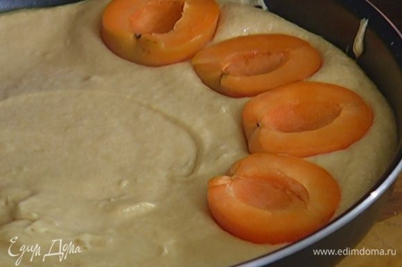 Выложить тесто в большую форму для выпечки, разровнять и разложить по всей поверхности абрикосы срезами вверх, слегка утопив их в тесте.