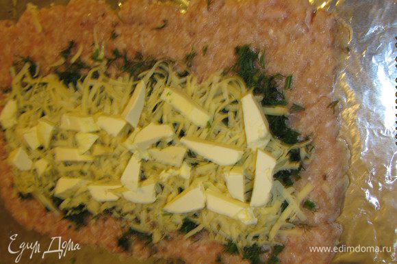 Сыр натираем на крупной терке и выкладываем поверх зелени. Масло, предварительно замороженное, нарезаем кусочками и выкладываем поверх зелени и сыра. При помощи фольги сворачиваем рулет.