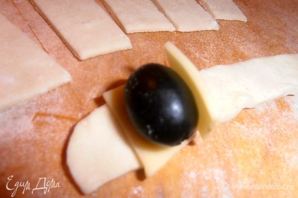 Каждую полоску делим пополам.На край теста кладём кусочек сыра,затем оливку боком и сверху снова сыр.