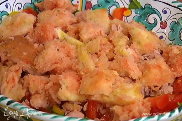 В блюдо с нарезанными овощами слоями выложить половину нарезанных помидоров, затем тунец и хлеб, вымоченный в соке помидоров.