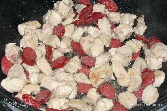Разогреть в сотейнике растительное масло и обжарить в нем кусочки курицы и колбасок, 5 минут.