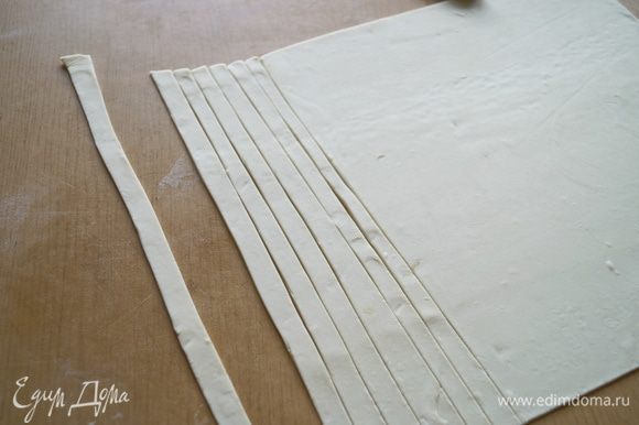 Готовое слоеное тесто разморозить и тонко раскатать, после чего нарезать длинными полосками шириной примерно 1 см.