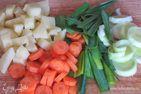Белую часть лука-порея нарезать колечками, зелёную-полосками. Морковь нарезать кружочками, картофель-ломтиками. Зелень мелко порезать.
