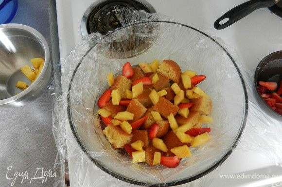 Скругленное блюдо застелить пленкой, оставив свешивающиеся края. Выложить на дно фруктово-ягодную смесь, затем слой из кусочков бисквита.