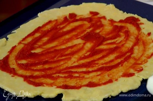 Раскатать тесто в тонкую лепешку, выложить ее на обратную сторону противня, смазать томатной пастой.
