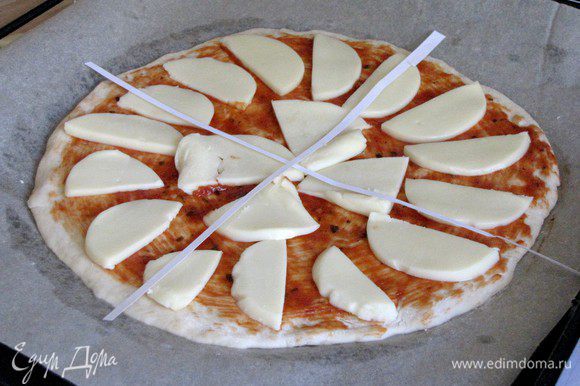 Выложить на тесто моцареллу. Из бумаги вырезать две полоски и выложить на пиццу в виде креста, формируя 4 сегмента.