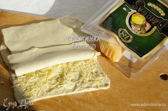 Сыр Джюгас натираем на мелкой тёрке. На одну половину теста распределяем сыр. Накрываем второй половиной. Раскатываем тесто в таком виде снова в прямоугольник по размеру, как в первый раз.
