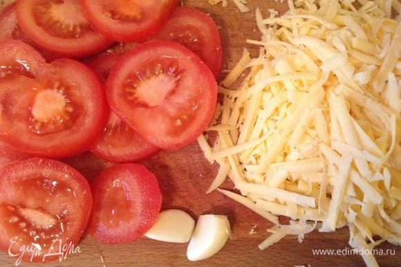 Тем временем порезать помидоры продольно, потереть сыр и очистить чеснок.