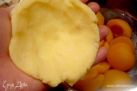 Каждый колобок положить на одну ладонь и прижать второй ладонью, чтобы образовалась лепешка. На каждую лепешку выложить по абрикосу, сложенному из двух половинок и начиненному кусочком сахара.