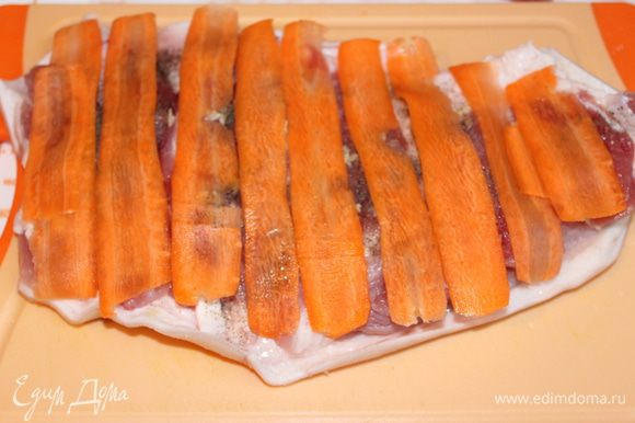Нарезаем тонко сырую морковь, при помощи овощечистки. Выкладываем полоски на рульку.