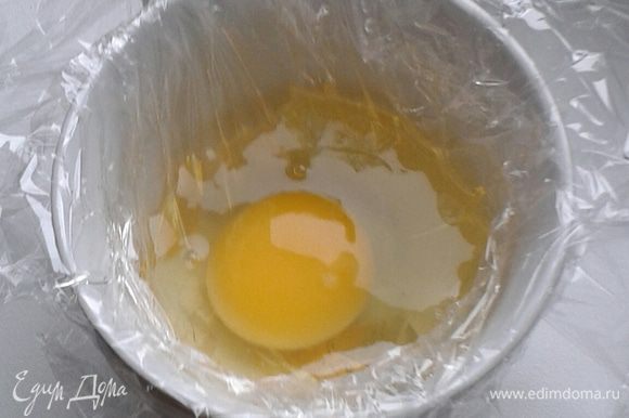 Смажьте пленку растительным маслом, затем осторожно разбейте яйцо и вылейте его в кружку.