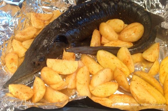 Картофель порезать на четвертинки, смешать со специями. Выложить рыбу и картофель на противень с фольгой.