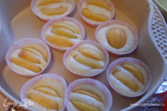 В формы для кексов выложить тесто, сверху слегка вдавить дольки абрикосов. Выпекать при 200 °C около 20 минут.