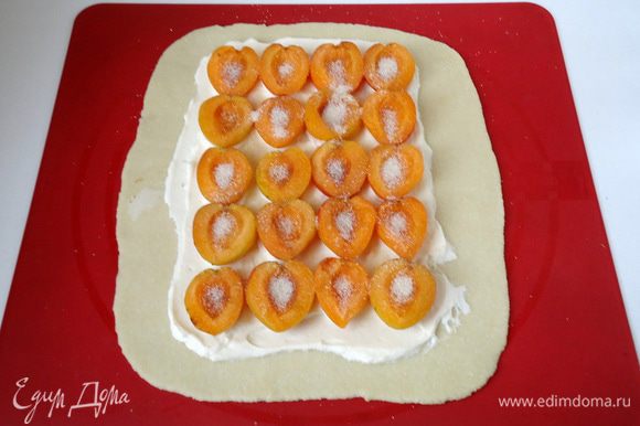 Не доходя до краев теста нанести смесь из крем - чиза и плавленого сыра, сверху выложить половинки абрикоса, присыпать его сахаром.