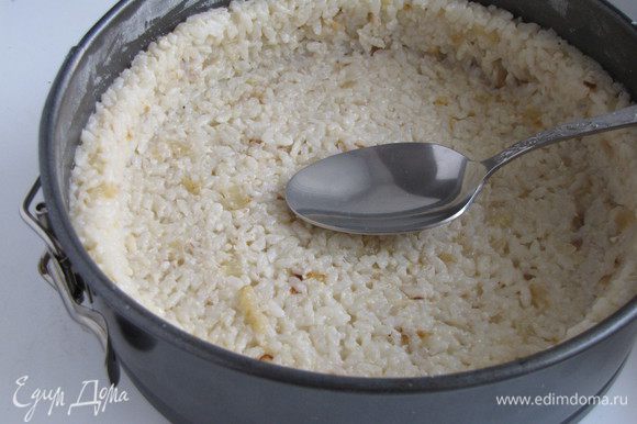 Разъемную форму диаметром 20 см смазать сливочным маслом, присыпать манкой или мукой. Выложить рис, формируя бортики при помощи ложки.