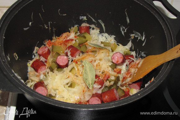За 15-20 минут до готовности капусты, добавить томатную пасту, нарезанный соленый огурец и охотничьи колбаски. Перемешать.