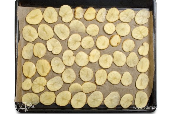 Картофель тщательно помыть, нарезать тонкими кружками и выложить на противень, застеленный бумагой для выпечки.