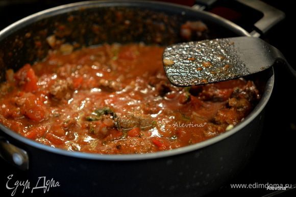 Добавить томаты баночные порезанные кубиками, изюм белый, вино, томатную пасту, сахар, базилик, соль и черный перец. Довести до кипения. Убавить огонь и тушить без крышки 15 минут.