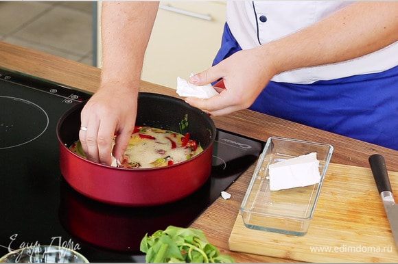 Фету нарезать маленькими кубиками и выложить на яйца с овощами. Накрыть крышкой и жарить фриттату до готовности.