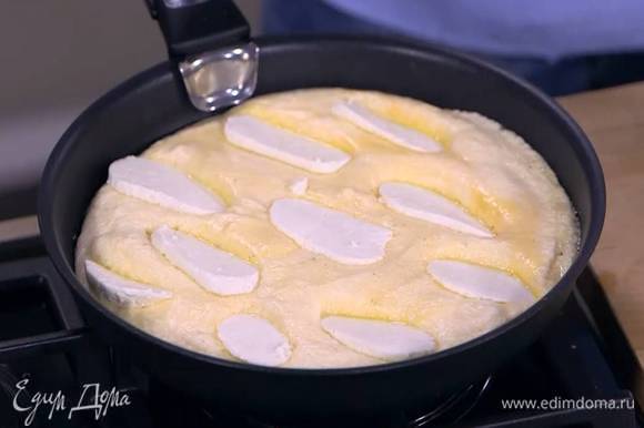Разогреть в сковороде сливочное масло, выложить яичную массу, разровнять ее, сверху поместить ломтики козьего сыра и накрыть сковороду крышкой.