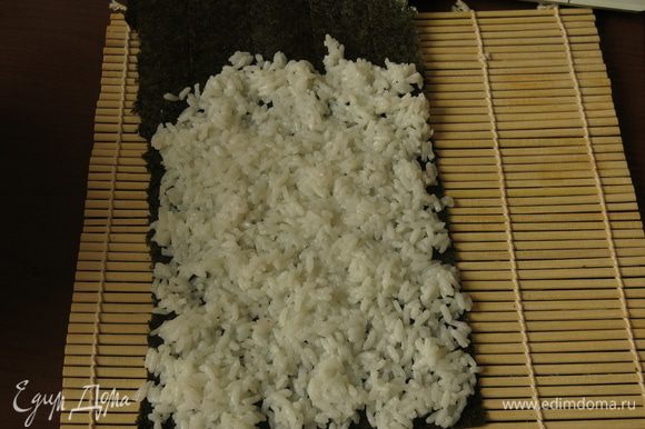 Выкладываем рис на нори так, чтобы обхватить по кругу рулет из омлета.