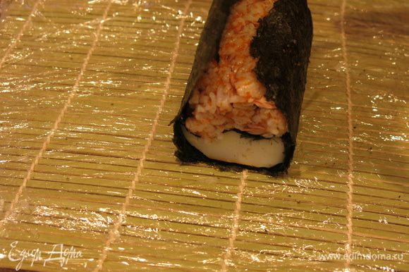 Поднимаем листы нори от края к центру, так, чтобы сохранить положение цветного риса над кальмаром, внутри получается фигура овал.