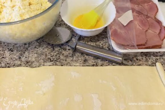 Духовку нагреть до 190°С. Сыр натереть на крупной терке, добавить белок и хорошо перемешать. Желток смешать с молоком. Слоеное тесто разделить на три части.