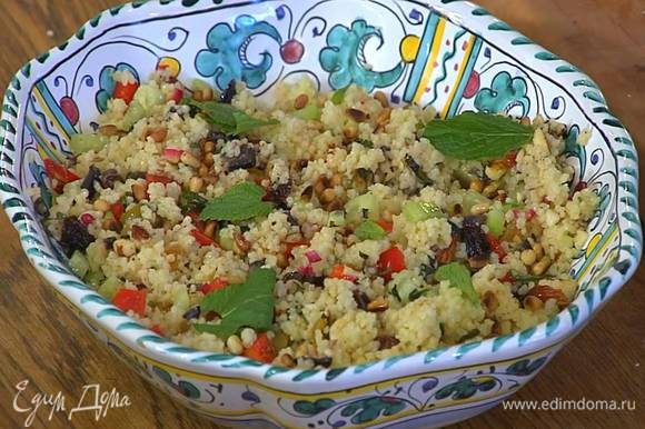 Кускус с овощами и орехами полить заправкой, перемешать и выложить на блюдо, посыпать кедровыми орехами, полить оставшимся оливковым маслом Extra Virgin и украсить оставшимися листьями мяты.