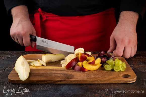 Нарежьте фрукты небольшими кусочками. Ягоды винограда разрежьте пополам и удалите косточки.