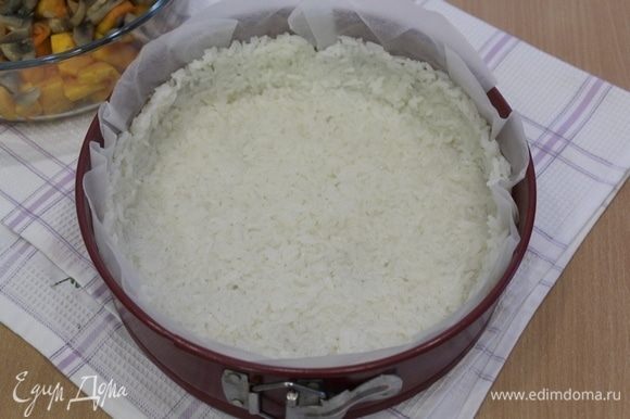 Рис уложите в форму, выложенную бумагой для выпечки, утрамбуйте по дну и бортикам формы.