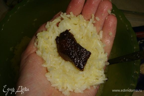 Берем столовую ложку риса, утрамбовываем его в руке в форме лепешки, кладем кусочек мяса, сверху еще немного риса и формируем шарик, прижимая рис руками. После каждого колобка смачиваем руки в воде.