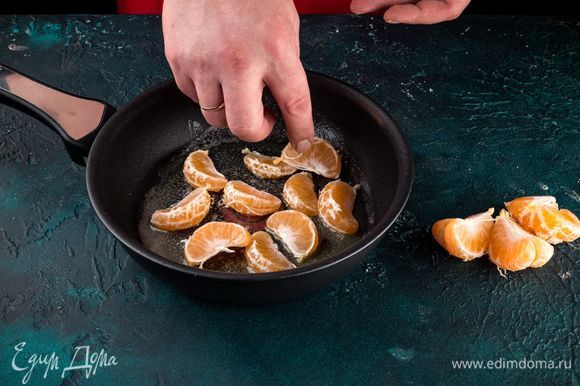 Когда мандариновые дольки подсохнут, в сковороде разогрейте немного масла, посыпьте его ложкой сахара и добавьте мандарины. Цитрусы обжарьте с двух сторон по 2 минуты.