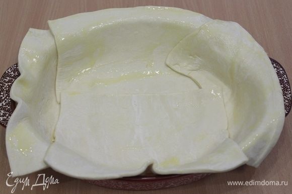 Слоеное тесто выложить в форму, так чтобы края свисали, смазать сливочным маслом.