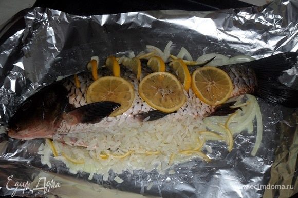 Поверх лука укладываем рыбу. Начиняем ее подготовленной рисово-луковой начинкой. В прорези вкладываем ломтики лимона.