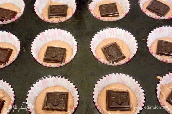 В бумажные формы для кексов положить часть теста. На нее положить кусочек шоколада.