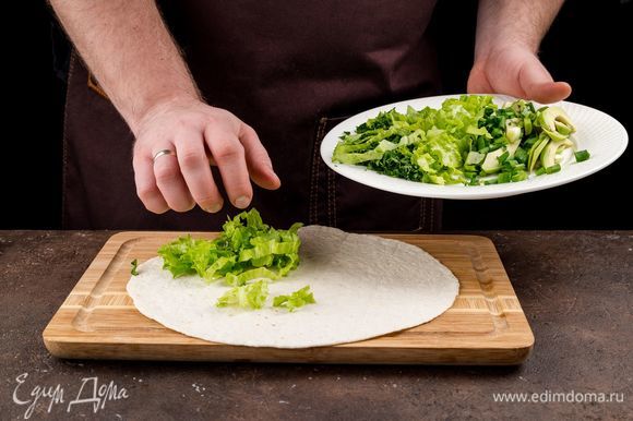 Приступаем к сборке кесадильи. Тортилью предварительно подогрейте на сковороде или в микроволновке. Положите тортилью на доску. На лепешку выложите зелень.